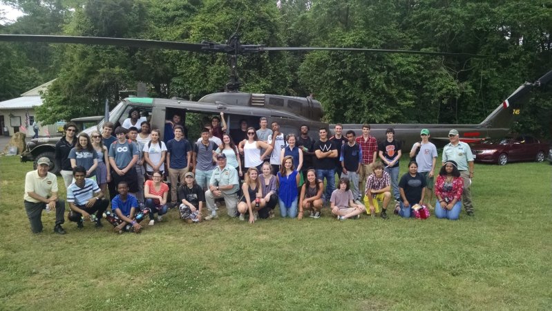 group of students standing on a lawn in from of a helicopter