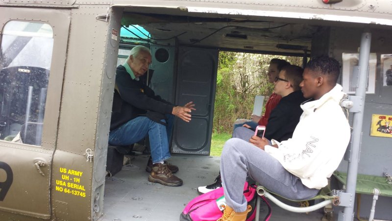 man inside immobile helicopter talking to several students