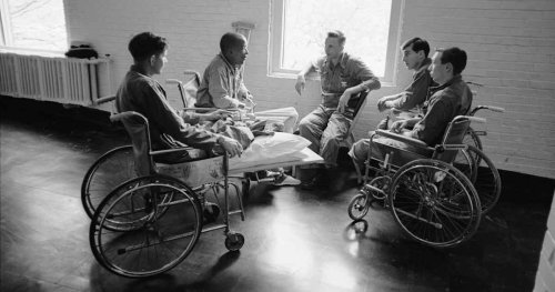 black & white photo of a group of 5 men, 4 of whom are in wheelchairs and one in a regular chair